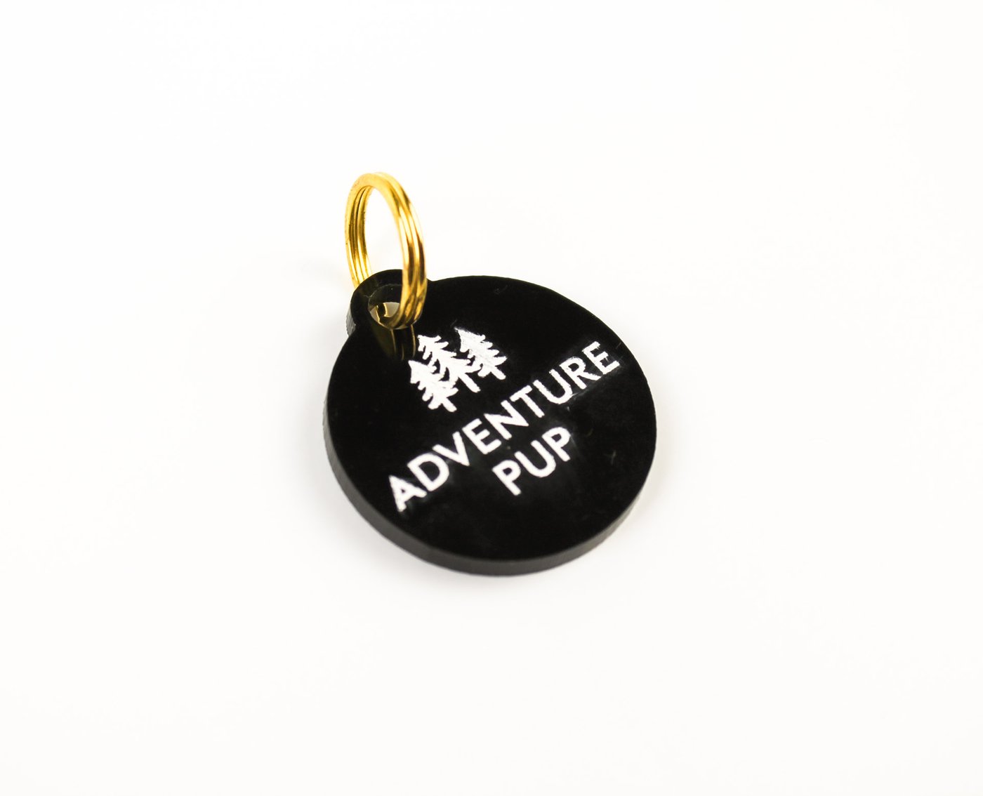 black acrylic adventure pup with trees dog tag with gold ring and white background
