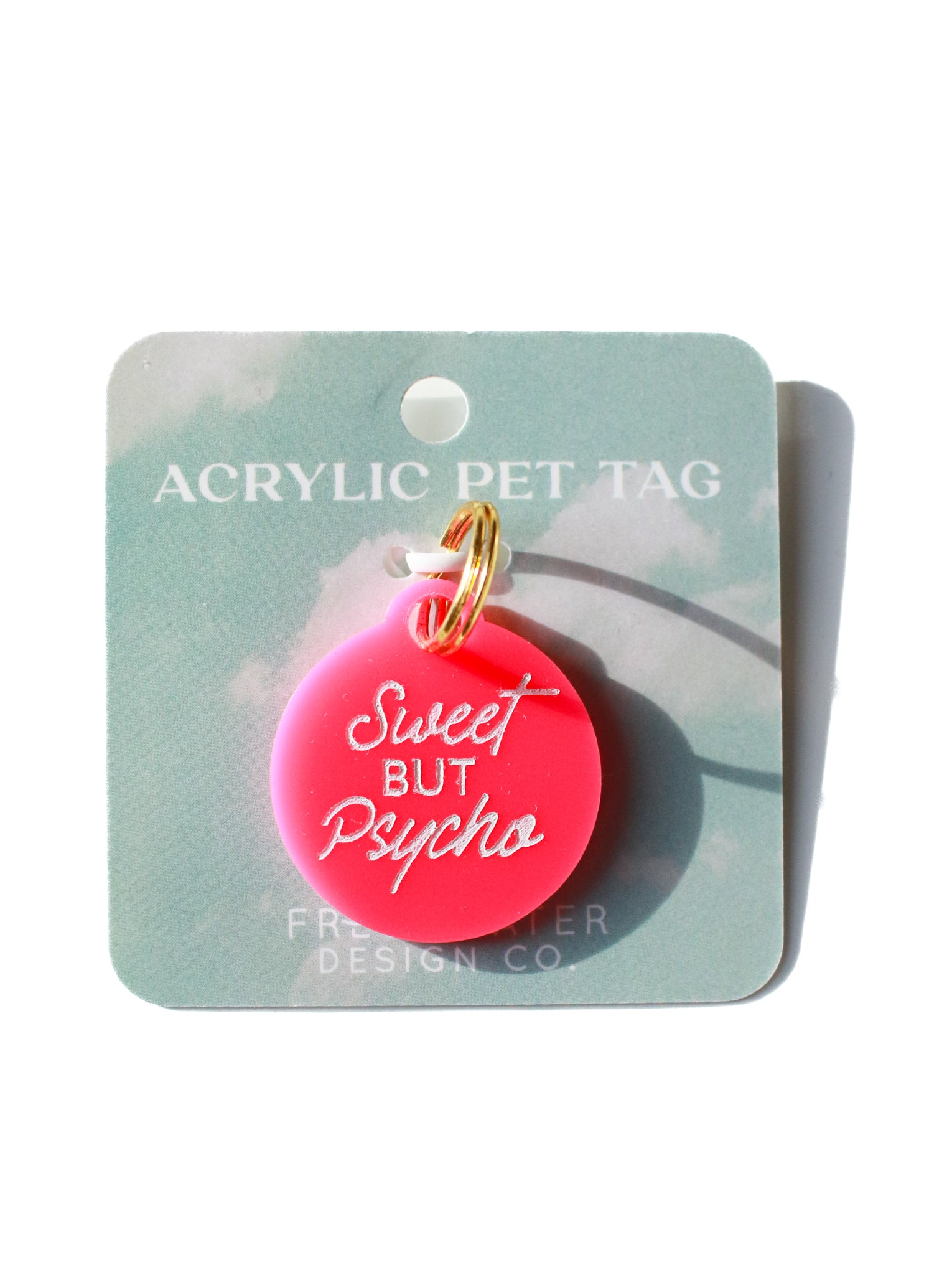 pink circle dog tag with white sweet but psycho lettering on white backdrop